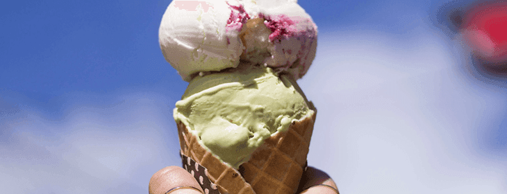 A hand holds a cone with green, white, and pink scoops of ice cream against a blue sky. A hand holds a cone with green, white, and pink scoops of ice cream against a blue sky.