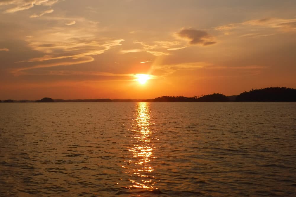 A lake with a beautiful sunset peeking through the clouds.