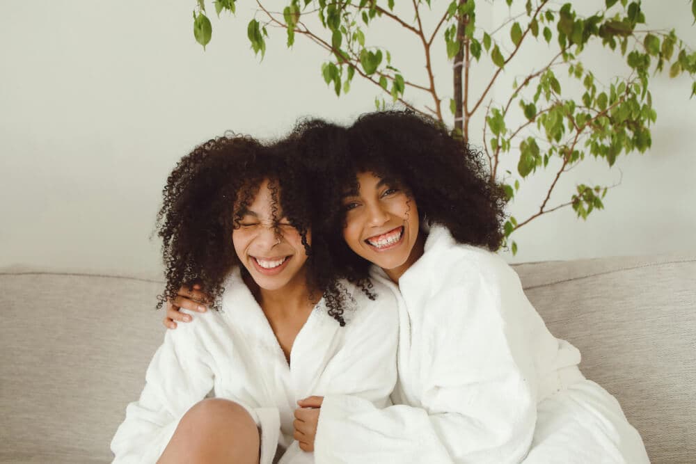 Two women in bathrobes smiling and laughing on a couch.