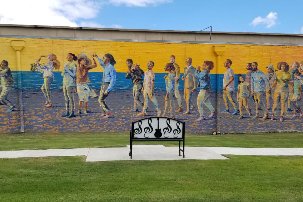 A colorful mural on the wall of a building with a lot of people on the beach laughing and playing music.