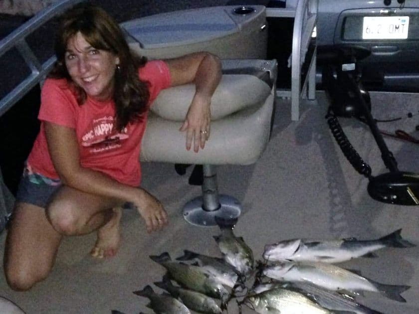 A woman kneels on a boat next to a pile of freshly caught fish. A woman kneels on a boat next to a pile of freshly caught fish.