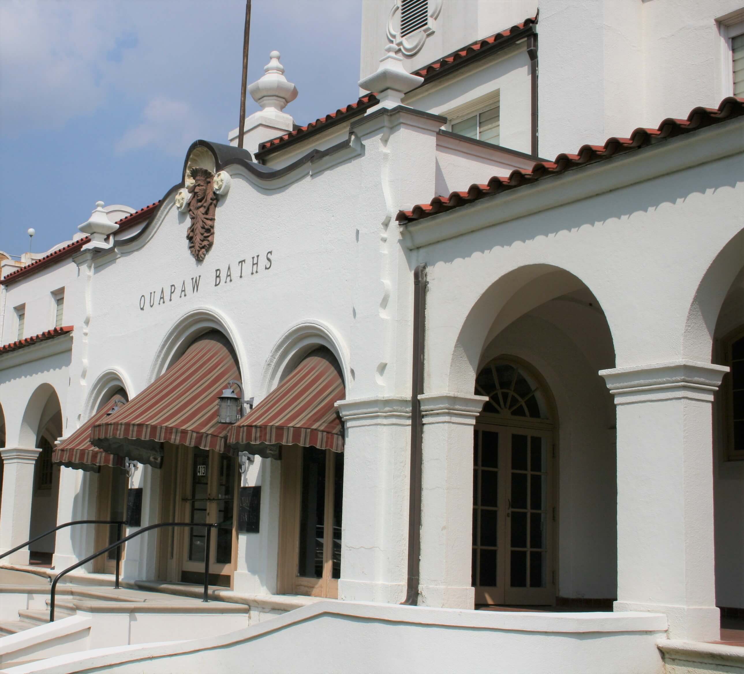 Exterior of the Quapaw Baths building featuring arched entrances and a red-striped awning. Exterior of the Quapaw Baths building featuring arched entrances and a red-striped awning.