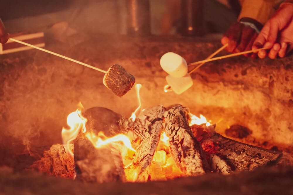 An outside fire pit with people roasting marshmallows.
