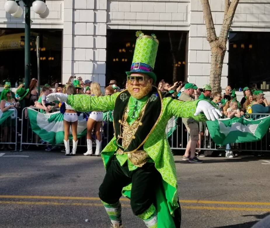 man dressed as a leprechaun standing with his arms spread out. Dallas Cowboys cheerleaders are behind him