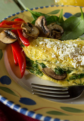 Breakfast plate of an omelet with fresh peppers and mushrooms and a side of baby spinach.