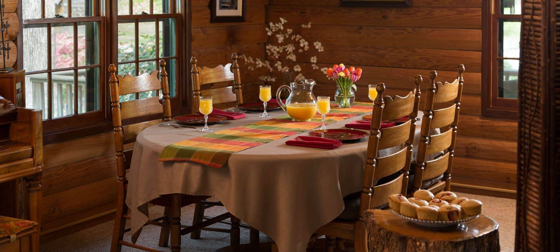 Dining room table set for four people with tan linens and multi colored napkins, orange juice and fresh flowers.