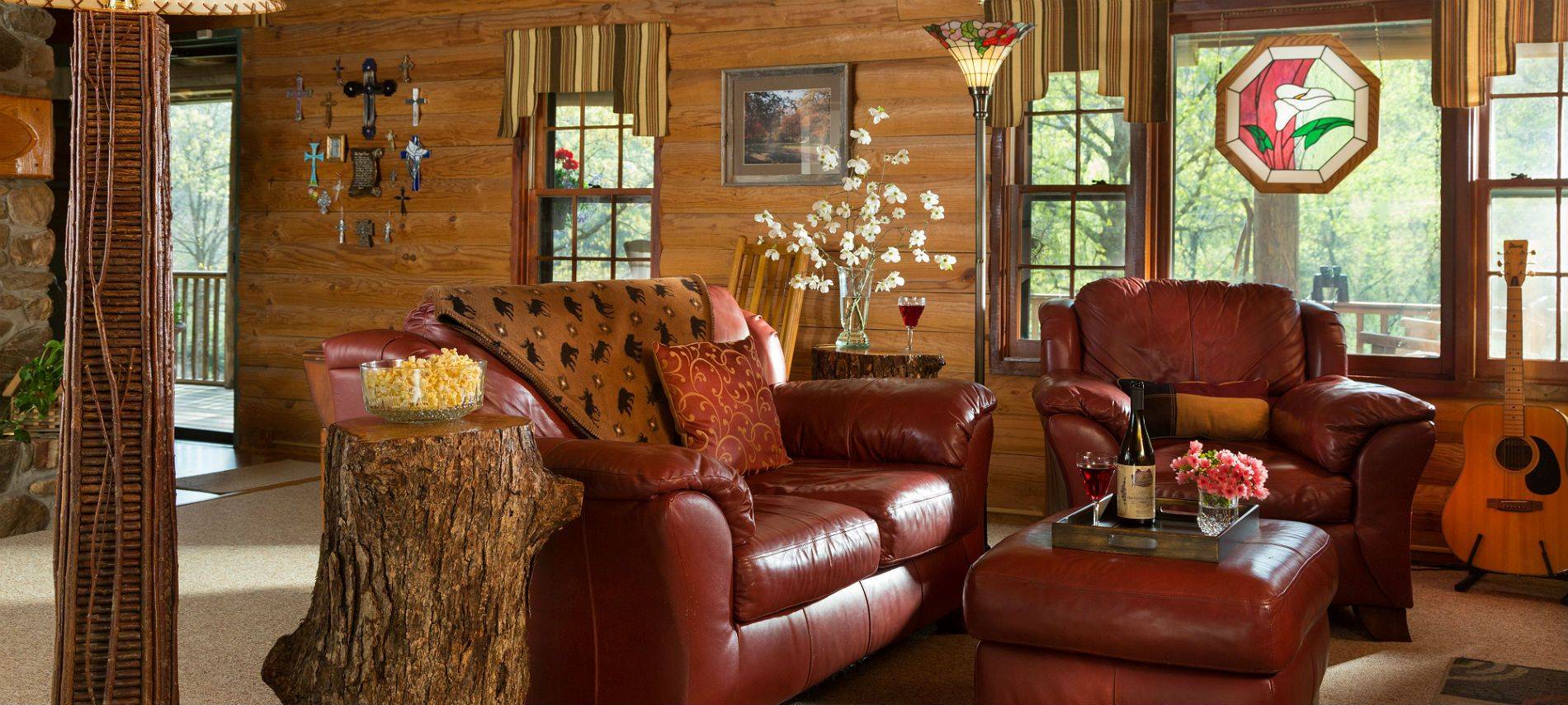 Leather sofa a side chair in a living room with log walls, rustic decor, stained glass floor lamp and window accent.