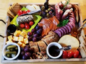 charcuterie board with assorted meats, cheeses, crackers, bread, olives, cornichons fruit, grape tomatoes, and condiments artfully displayed on a wooden tray