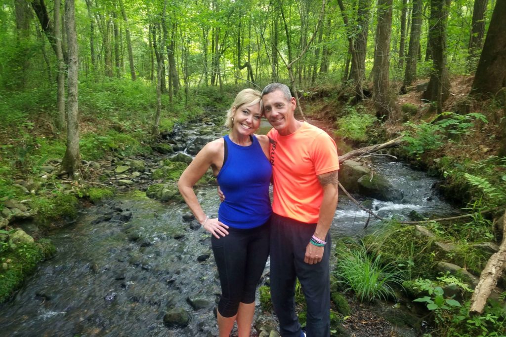 a man and woman standing together in frotn of a creek with trees in the background