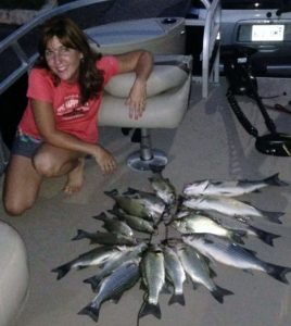 A circle of fish on the floor of a boat beside a very happy fisherwoman