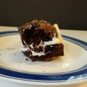 a roasted marshmallow sandwiched between 2 brownies on a blue and white plate